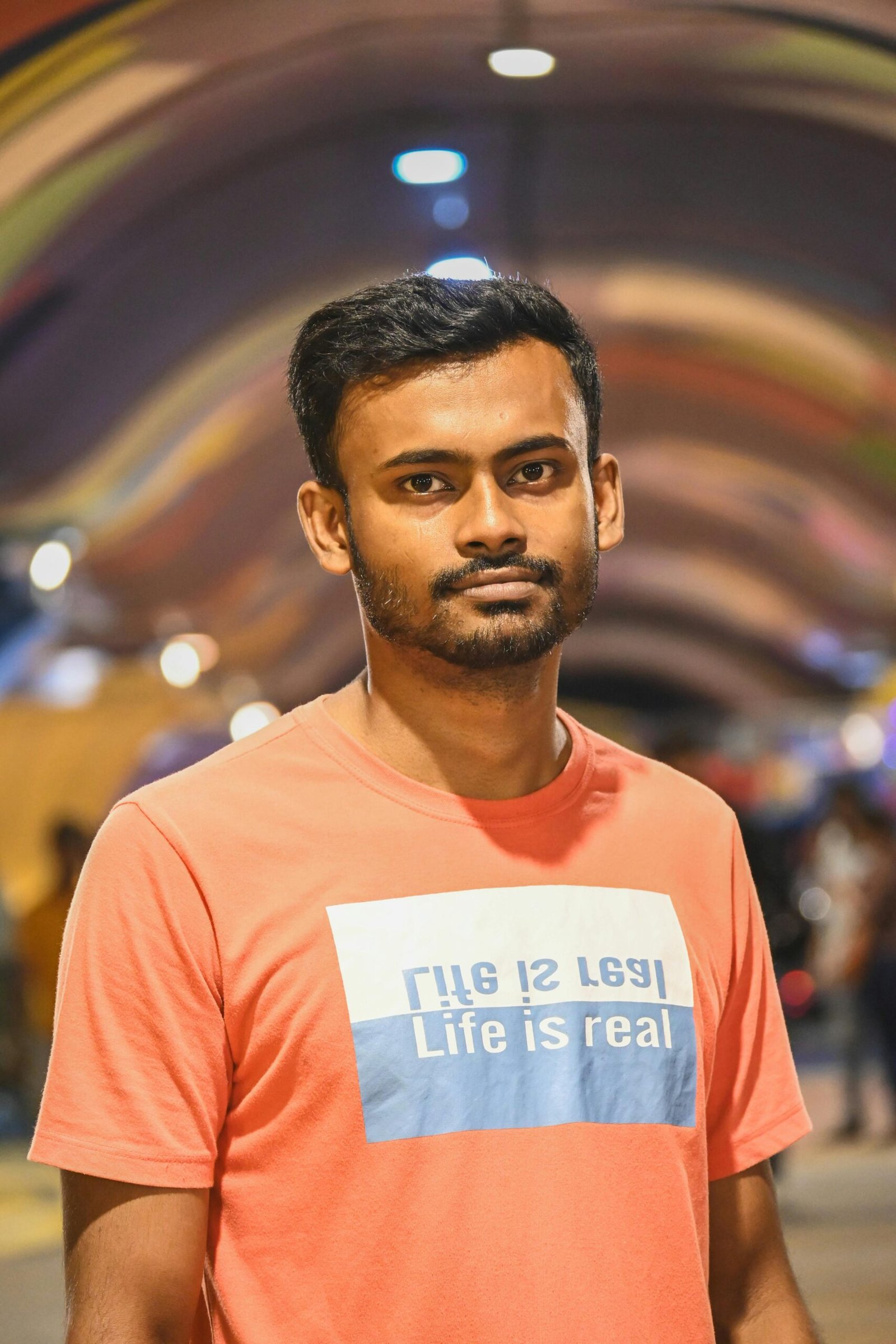 Portrait of a young man standing in a colorful urban tunnel during nighttime.